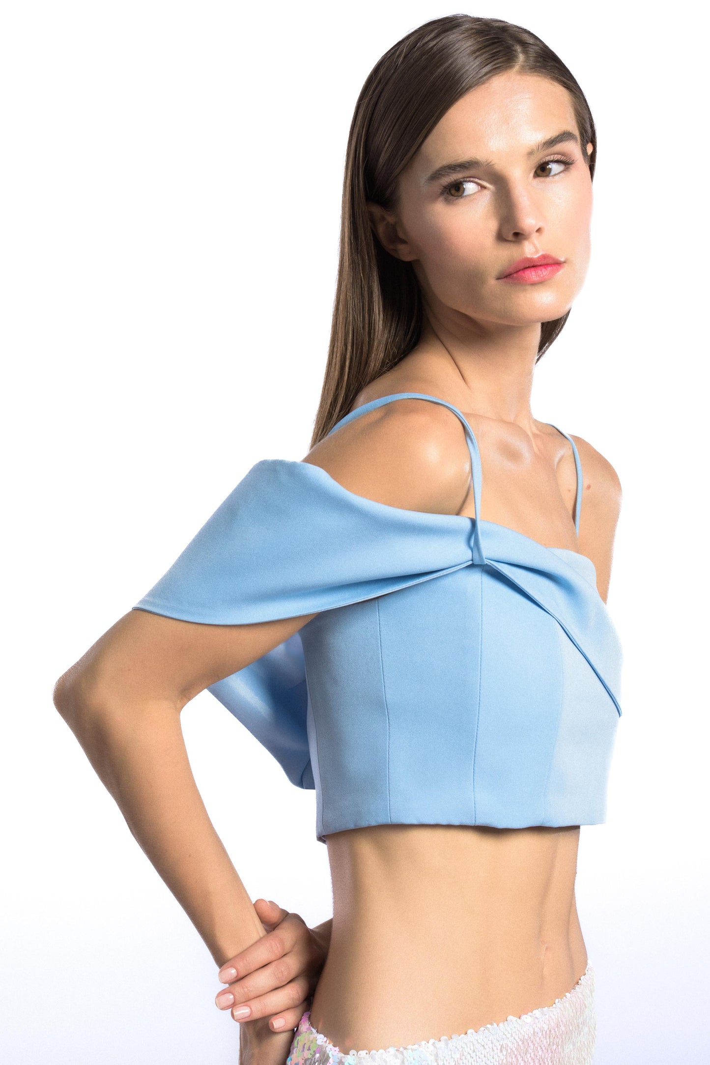 Model wearing asymmetric off shoulder crepe crop top in pastel blue color and iridescent sequins mini skirt