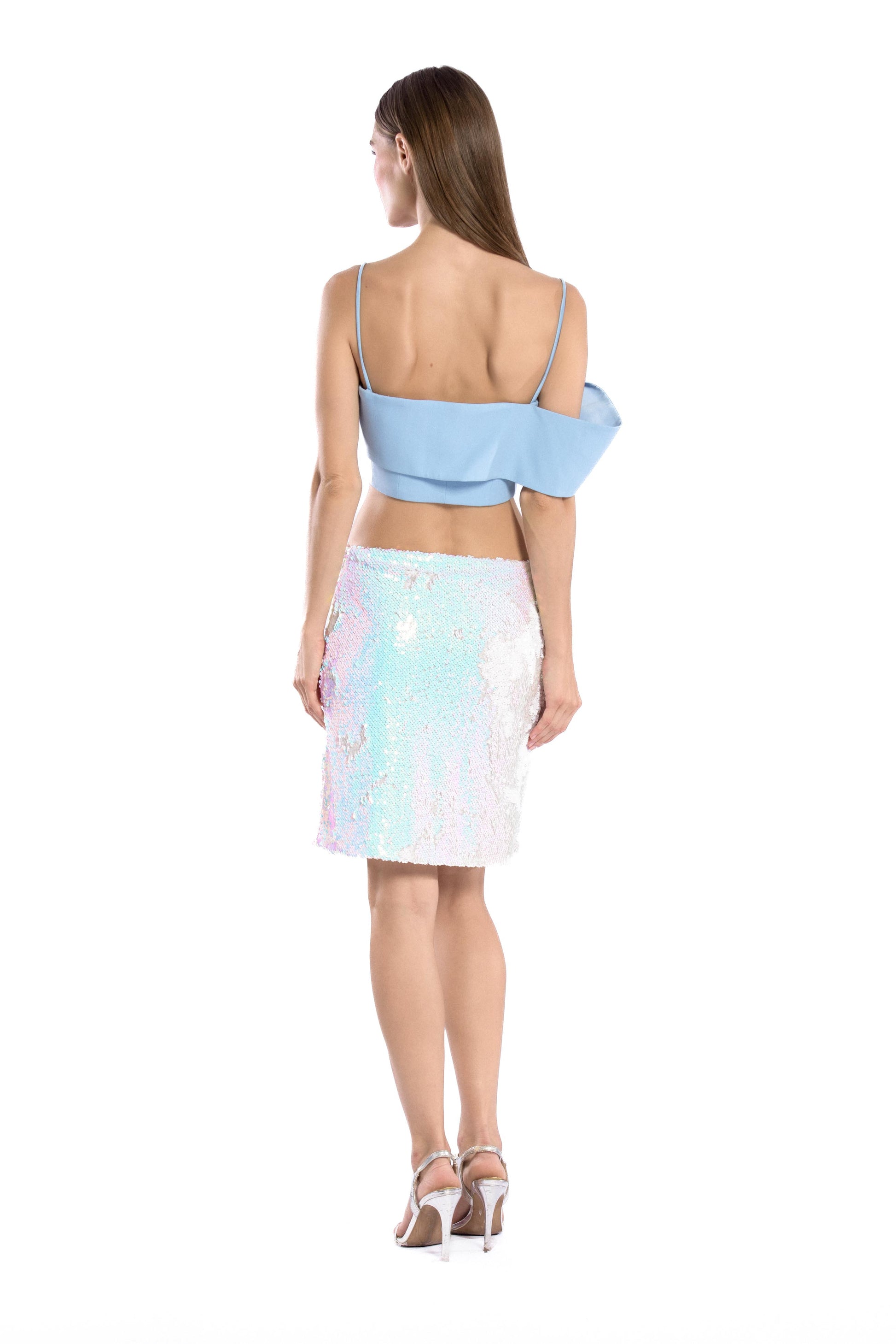 Back shot of model wearing asymmetric off shoulder crepe crop top in pastel blue color and iridescent sequins mini skirt