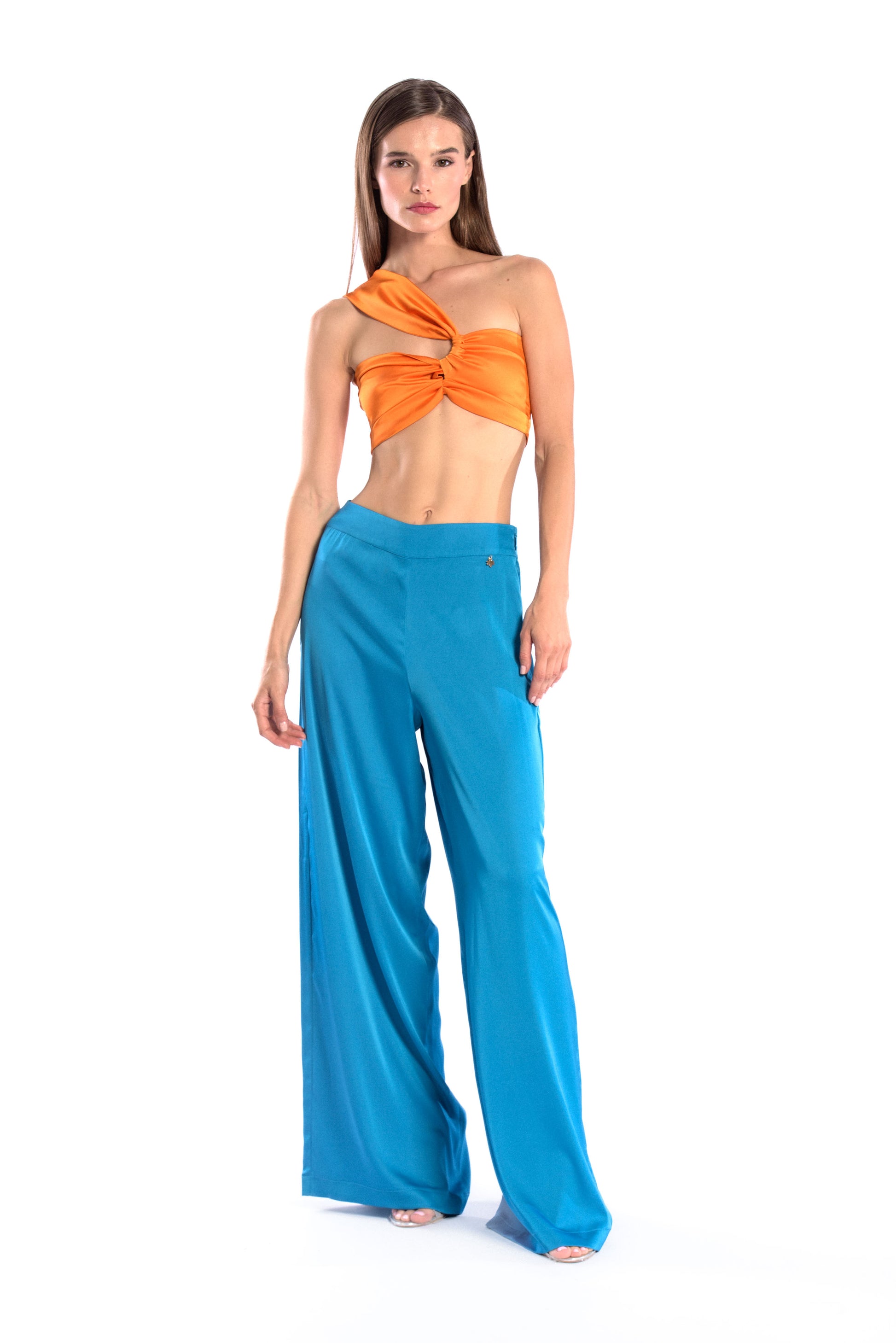 Model wearing a silk cross shoulder crop top in orange with back firefly logo golden zipper and silk pants in blue color with a firefly golden charm