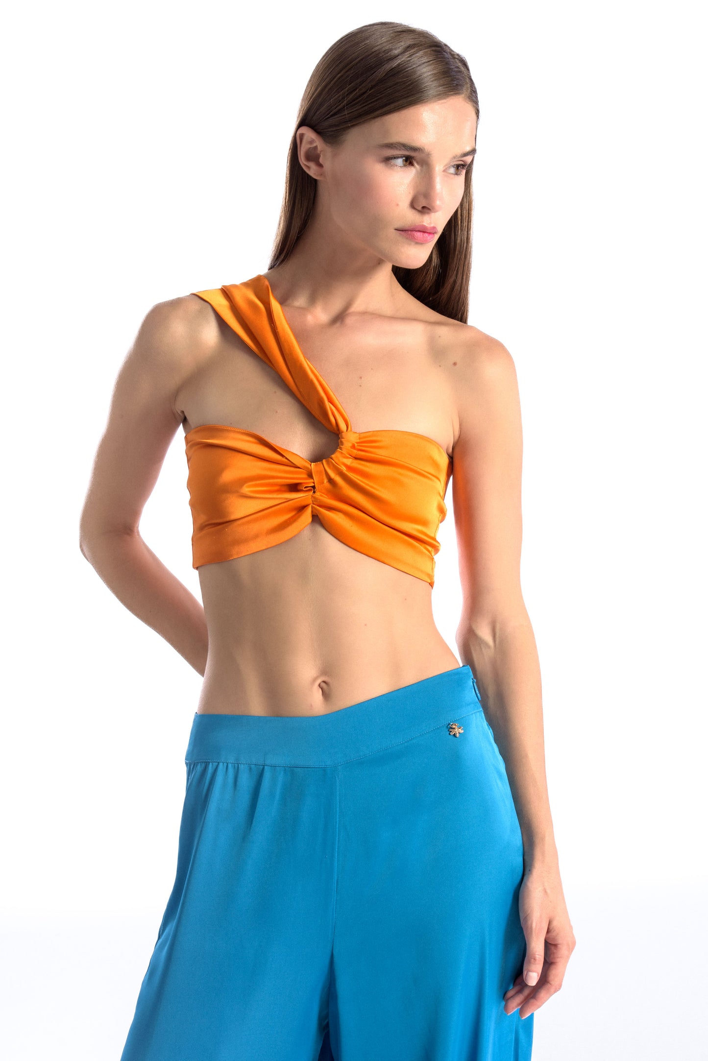 Model wearing a silk cross shoulder crop top in orange with back firefly logo golden zipper and silk pants in blue color with a firefly golden charm