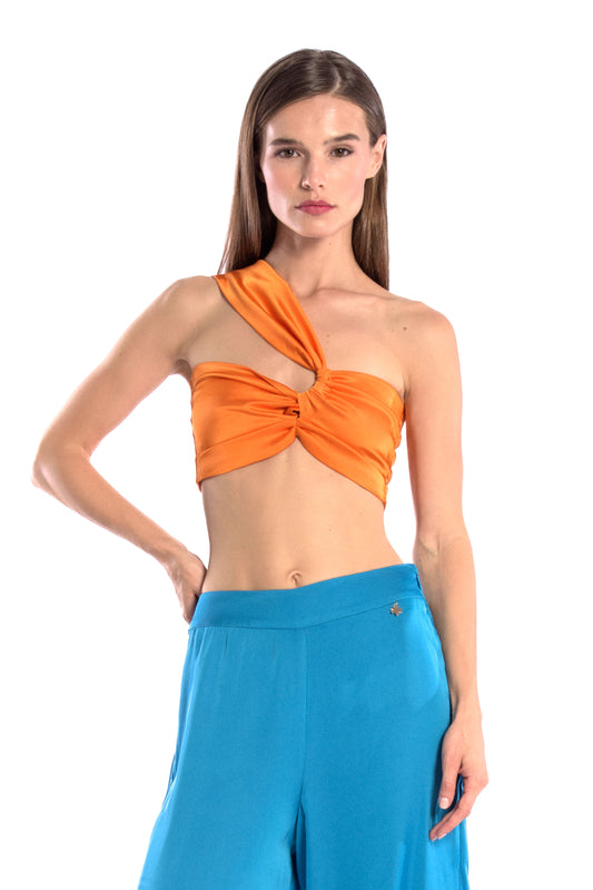 Model wearing a silk cross shoulder crop top in orange with back firefly logo golden zipper and silk pants in blue color with a firefly golden charm
